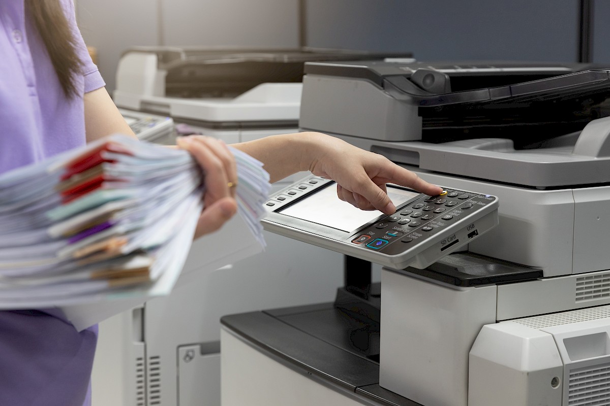 Bussiness woman using copier machine to copy heap of paperwork in office.